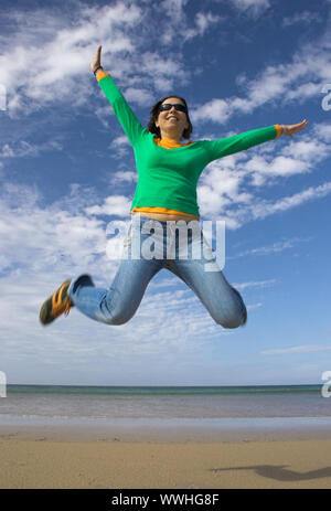 Junge schöne Frau, die einen grossen Sprung am Strand Stockfoto