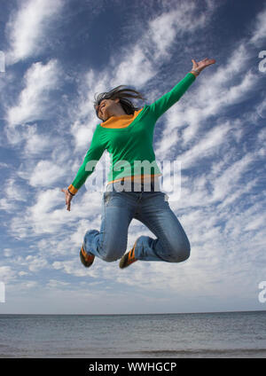 Junge schöne Frau, die einen grossen Sprung am Strand Stockfoto