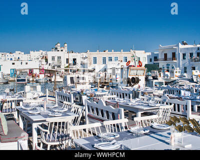 Einsame open air Restaurant mit weißen serviert Tabellen und angelegten Boote im alten Hafen von Naoussa Griechenland unter blauem Himmel Stockfoto