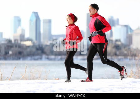 Läufer laufen im Winter Schnee mit Sicht auf die City Skyline im Hintergrund. Gesunde multirassischen junges Paar. Asiatische Frau runner und kaukasischen Mann laufen mit Montr Stockfoto