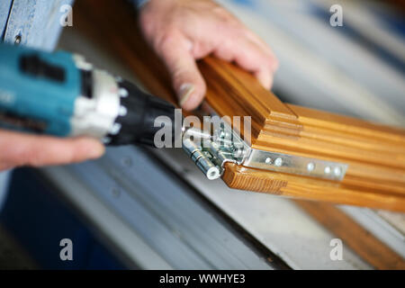 Hände eines Tischlers verschraubt ein Scharnier auf eine Holztür Stockfoto