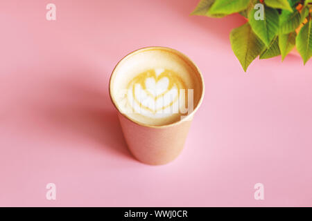 Blick von oben auf die Kaffee mit Latte Art mit grünen Blättern auf rosa Hintergrund zu gehen. Stockfoto