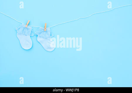 Paar blauen Cute Baby Socken hängen auf der Wäscheleine auf blauem Hintergrund. Baby Accessoires. Flach. Stockfoto