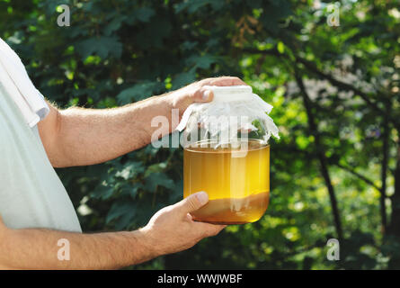 Mann mit einem Glas Glas mit Tee Pilz hausgemachte kombucha Tee im Garten gefüllt. Gegorene Getränke, Kaffee gesunden natürlichen probiotic im Glas. Stockfoto