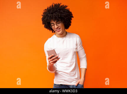 Junge schwarze Mann mit Smartphone auf Orange Studio Hintergrund Stockfoto