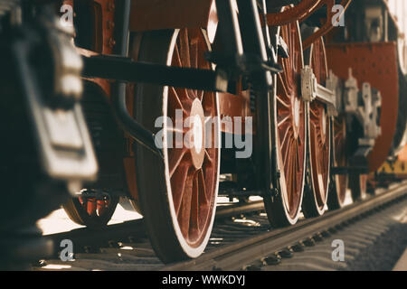 Ein vintage Foto des Roten große Räder eines alten aus dem 20. Jahrhundert Lokomotive, die auf Schienen steht, die durch Sonnenlicht beleuchtet. Stockfoto