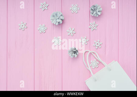 Weihnachtsgeschenk verpacken Hintergrund. Flach mit weißen Handwerk Paket und Kegel und Schneeflocken auf rosa Holz- Hintergrund. Moderne Komposition in Stockfoto