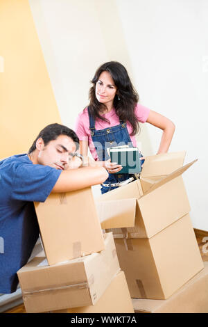 Junger Mann schlafen beim Auspacken Boxen, mißbilligen Frau auf der Suche Stockfoto