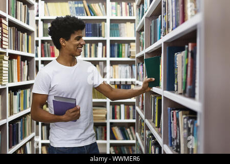 Stattlichen schwarzen Kerl auf der Suche nach Buch über Bücherregale in Bibliothek Stockfoto