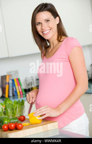 Schwangere Frau in der Küche machen einen Salat und lächelnd Stockfoto