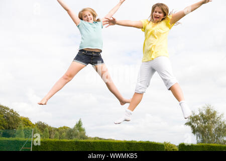 Zwei junge Mädchen springen auf dem Trampolin lächelnd Stockfoto
