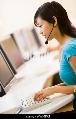 Frau trägt Kopfhörer sitzen in Computer Zimmer eingeben Stockfoto