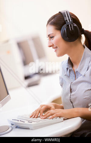 Frau mit Kopfhörern im Computerraum Typisierung und lächelnd Stockfoto