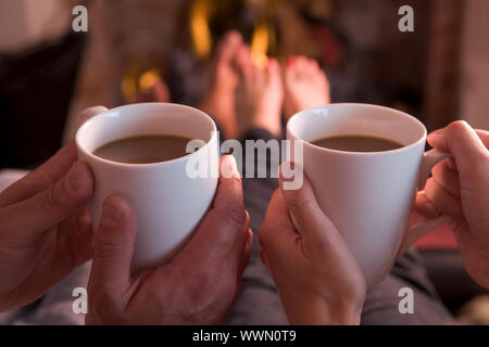 Füße mit Händen mit Kaffee am Kamin Erwärmung Stockfoto