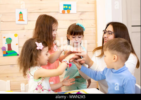 Kinder und Lehrer die Hände zusammen wie eine Mannschaft. Lektion in Vorschule und Kindergarten Stockfoto