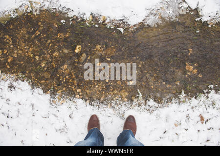 Menschliche Füße männlichen tragen Winter Stiefel und Jeans auf der Bank des kleinen Spring Creek bedeckt mit weißen sauberer, frischer Schnee Stockfoto