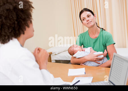 Arzt mit Laptop und Frau des Arztes Büro halten Baby Stockfoto