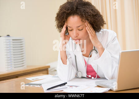 Arzt mit Laptop und Kopfschmerzen in Arztpraxis Stockfoto