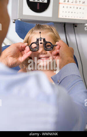 Optiker in Untersuchungszimmer mit jungen Mädchen im Sessel lächelnd Stockfoto