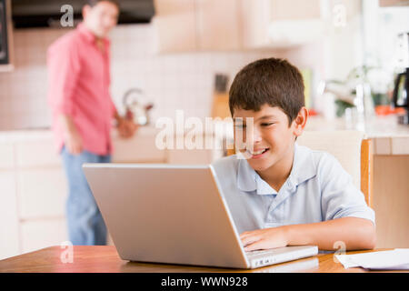 Junge in Küche mit Laptop und Unterlagen lächelnd mit Mann Stockfoto