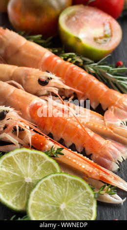 Rohe Langostinos mit Gemüse und Kräutern auf dem dunklen Hintergrund Stockfoto