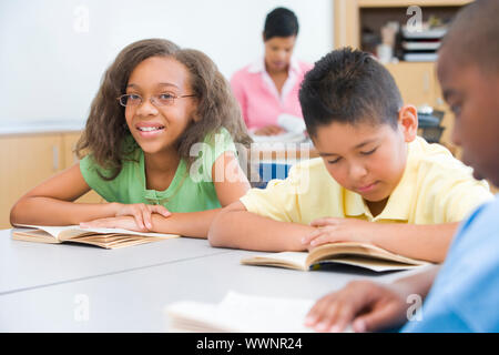 Gruppe von Schülerinnen und Schüler das Lesen von Büchern, während am Schreibtisch sitzen Stockfoto