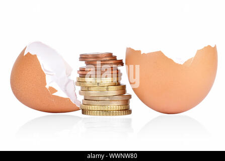 Eierschale mit Münzen zwischen auf einen weißen Hintergrund mit einem Schatten unter gebrochen Stockfoto