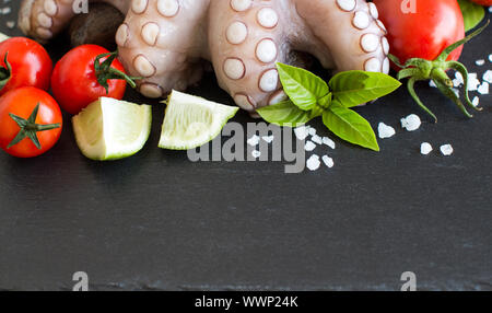 Rohen Tintenfisch mit Kalk, Tomaten und Basilikum über dunklen Hintergrund Stockfoto