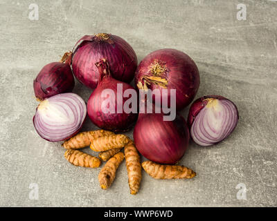 Close-up von oben. Rote Zwiebeln und Wurzeln von curcuma isoliert auf grauem Hintergrund. Eine in Scheiben geschnittene Zwiebel. Selektive konzentrieren. Stockfoto