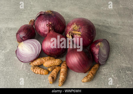 Close-up von oben. Rote Zwiebeln, die Wurzeln von gelbwurz isoliert auf grauem Hintergrund. Eine in Scheiben geschnittene Zwiebel. Selektive konzentrieren. Stockfoto