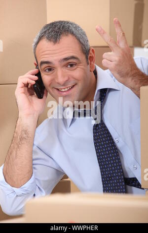 ein Business-Mann ruft jemand in einem Raum voller Kartons Stockfoto