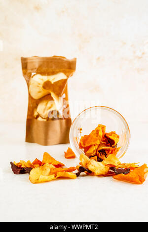 Gesunder Snack aus pflanzlichen Chips von rote Beete, Karotten, Pastinaken in einem Glas, braunes Papier Paket auf hellen Hintergrund Stockfoto