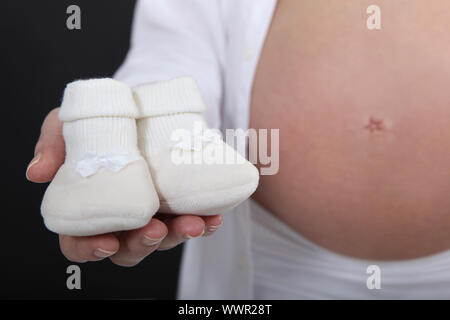 Schwangere Frau hält ihr ungeborenes Baby Hausschuhe Stockfoto