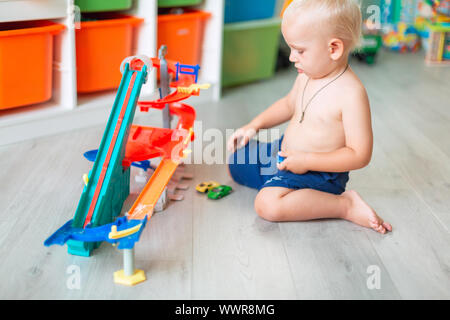 Cute Baby Boy spielen mit Spielzeug Autos auf Schiene in der Kid's Zimmer Stockfoto