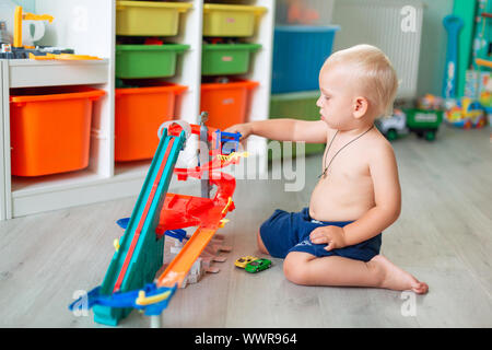 Cute Baby Boy spielen mit Spielzeug Autos auf Schiene in der Kid's Zimmer Stockfoto