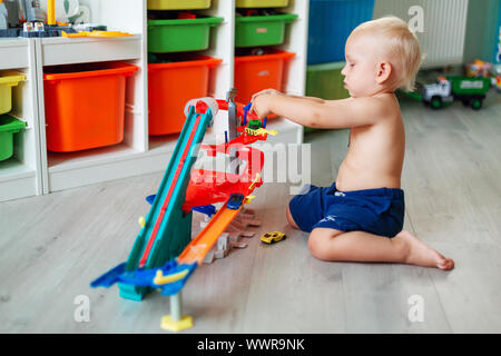 Cute Baby Boy spielen mit Spielzeug Autos auf Schiene in der Kid's Zimmer Stockfoto