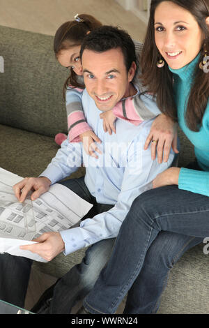 Junge Familie entspannend auf Sofa mit Zeitung Stockfoto