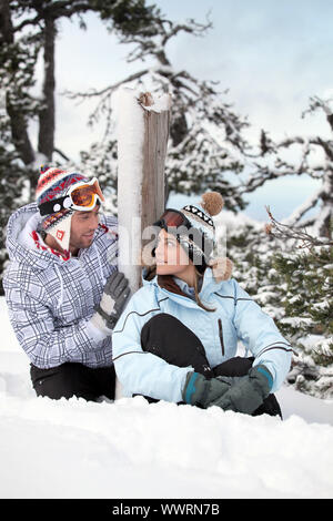 Junges Paar saß auf dem Schnee Stockfoto