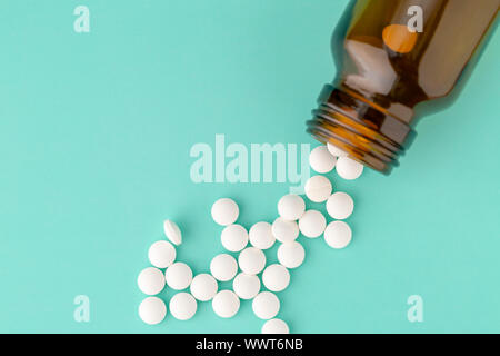 Weiße, runde Tabletten vor Glas Flasche Pillen verstreut Stockfoto