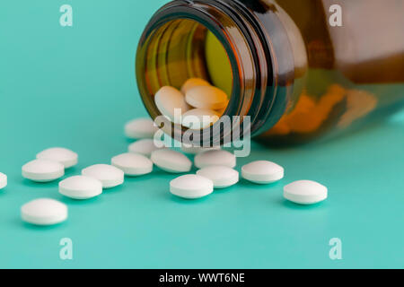 Weiße, runde Tabletten vor Glas Flasche Pillen verstreut Stockfoto