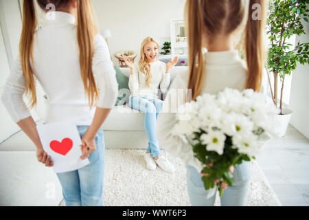 Schöne schöne attraktive charmante Fröhliche positive fröhlich vor - jugendlich Mädchen verstecken Geschenke für Mama mama Mama sitzen auf divan Veranstaltung daydream in Weiß leuchtet Stockfoto