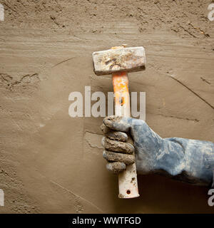 Hammer Mann Hand mit Handschuhen in Grunge-Zement-Mörtel-Hintergrund Stockfoto
