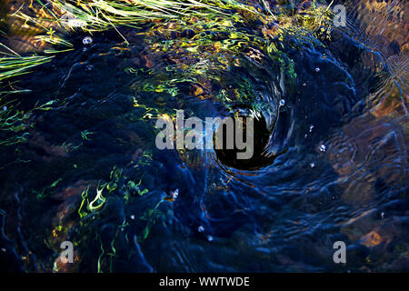 Blaues Wasser wirbeln in ein Loch im Boden Stockfoto