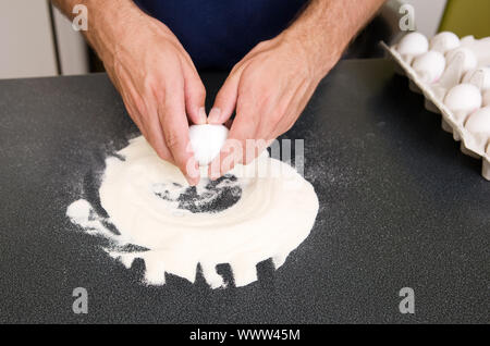 Ein junger Mann, Pasta in einer Wohnung Küche - Risse ein Ei in das Mehl von Hand auf der Theke gemischt werden Stockfoto