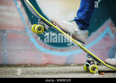 Skateboard stunt Training. Skateboard und Kinderfüße in Turnschuhen gegen Wand Hintergrund. Gesunder Lebensstil Konzept. Geringe Tiefenschärfe. Sele Stockfoto