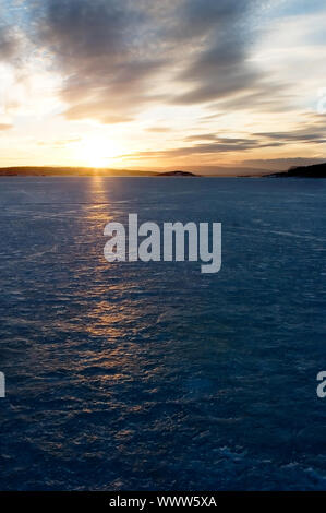 Einen goldenen Sonnenuntergang hinunter hinter einem Hügel über einen gefrorenen See-Fjord. Oslo Fjord im März. Stockfoto