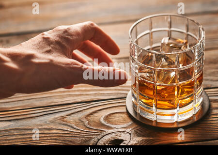 Die Hand des Mannes erreichen zu Glas Whisky mit Eiswürfel. Alkoholismus Konzept. Stockfoto