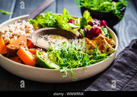 Buddha Schüssel mit Tofu, Avocado, Reis, Sämlinge, Süßkartoffel und tahini Dressing. Veganes essen Konzept. Stockfoto