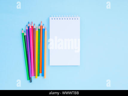 Bunte Bleistifte und ein Notebook auf blauem Hintergrund mit Copyspace. Flach Stil. Zurück zum Konzept der Schule. Stockfoto