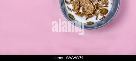 Minimalismus. Gesundes Frühstück Müsli mit Milch in einem grauen Schale auf einem rosa Hintergrund. Stockfoto
